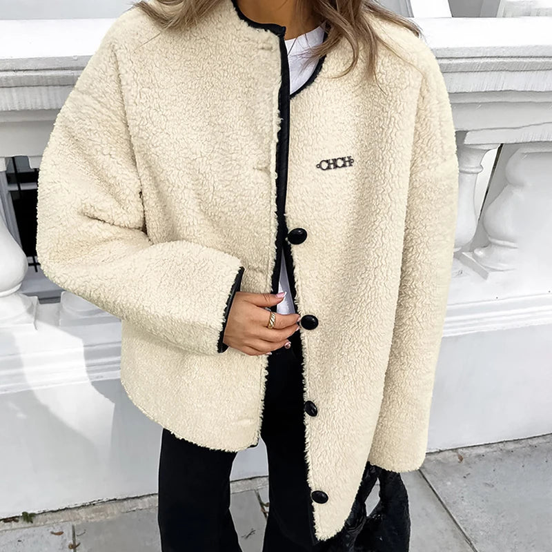 Person wearing a cream-colored jacket with black buttons and trim, standing on a street.