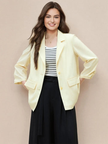 Woman wearing a light yellow blazer over a striped shirt and black skirt on a beige background