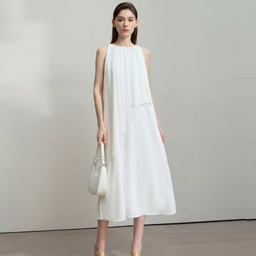 Woman wearing a white dress holding a handbag against a plain background