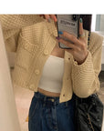 Person wearing a beige knitted cardigan, white top, and blue jeans taking a mirror selfie.