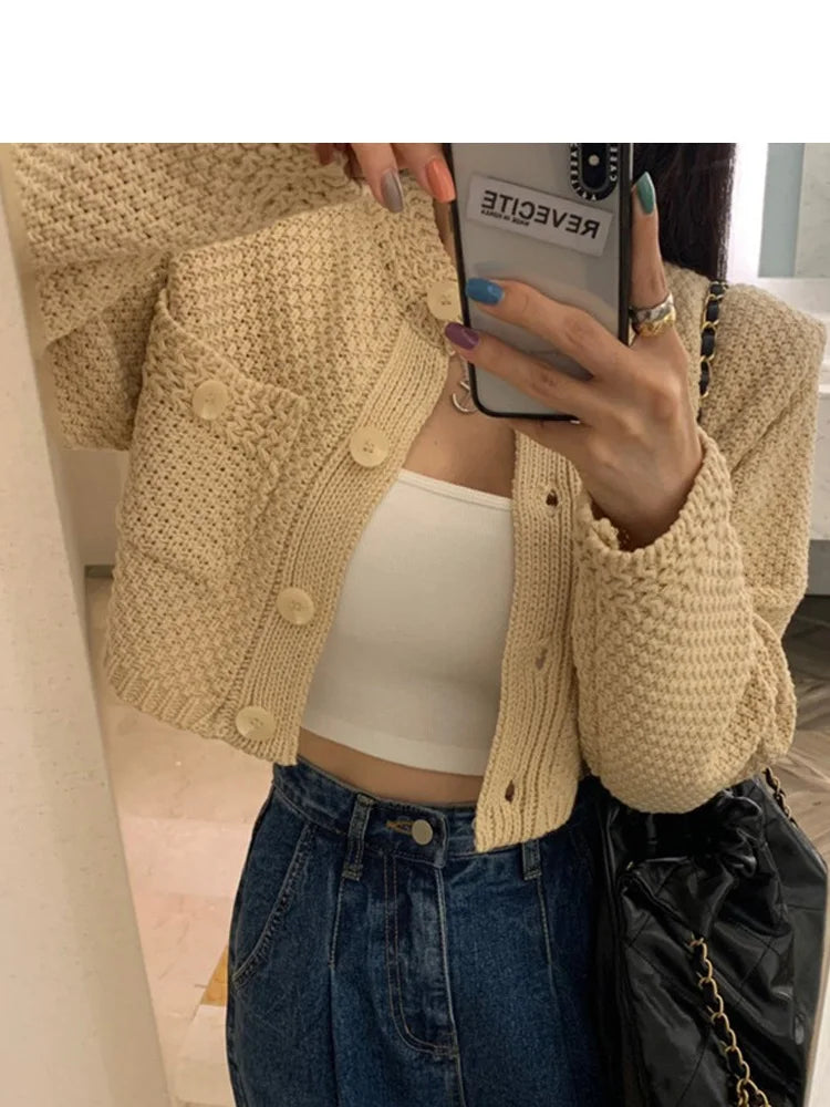 Person wearing a beige knitted cardigan, white top, and blue jeans taking a mirror selfie.