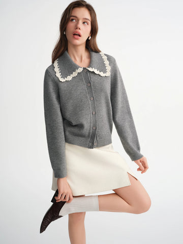 Woman wearing a gray cardigan with lace collar and white skirt on a light background