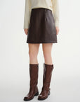 Person wearing a brown leather skirt and boots on a white background