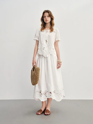Woman wearing a white lace dress holding a straw bag on a plain background