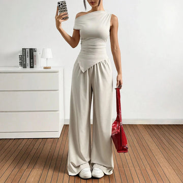 Person wearing a white outfit holding a red bag in a minimalistic room.