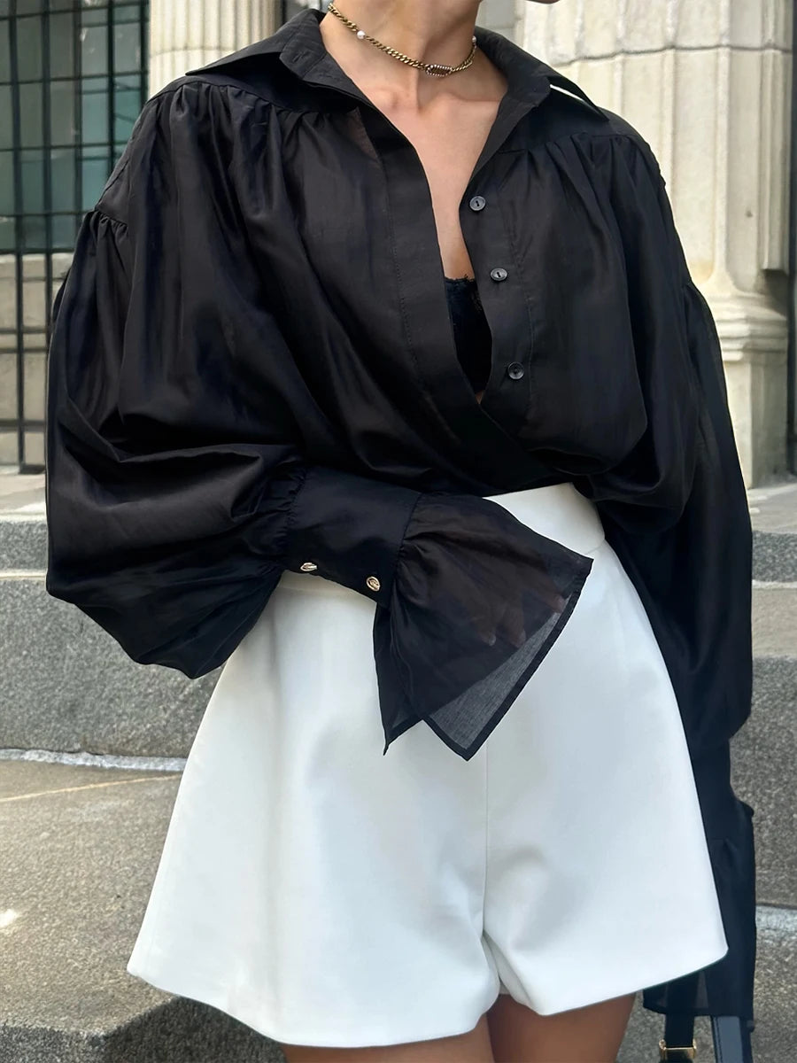Person wearing a black oversized shirt with a bow tie and white shorts outdoors.