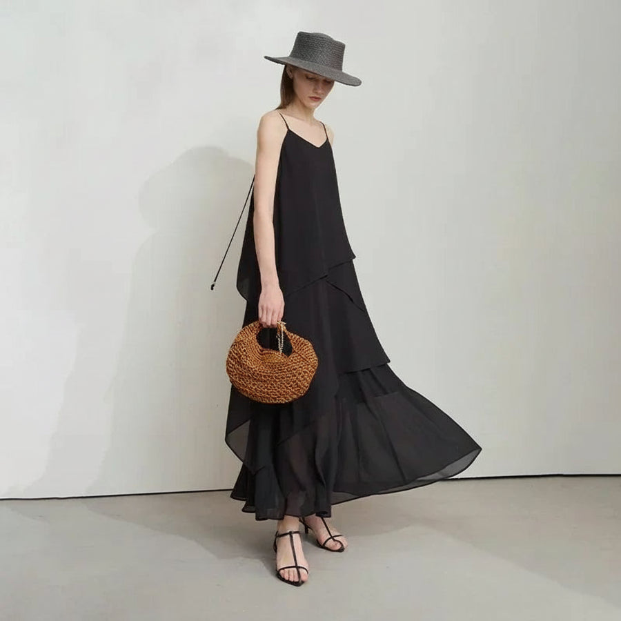 Woman wearing a black dress and hat, holding a woven bag, with AMII branding.