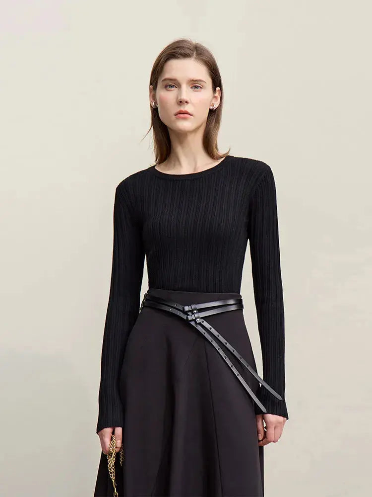 Woman wearing a black ribbed sweater and black skirt with a belt on a beige background