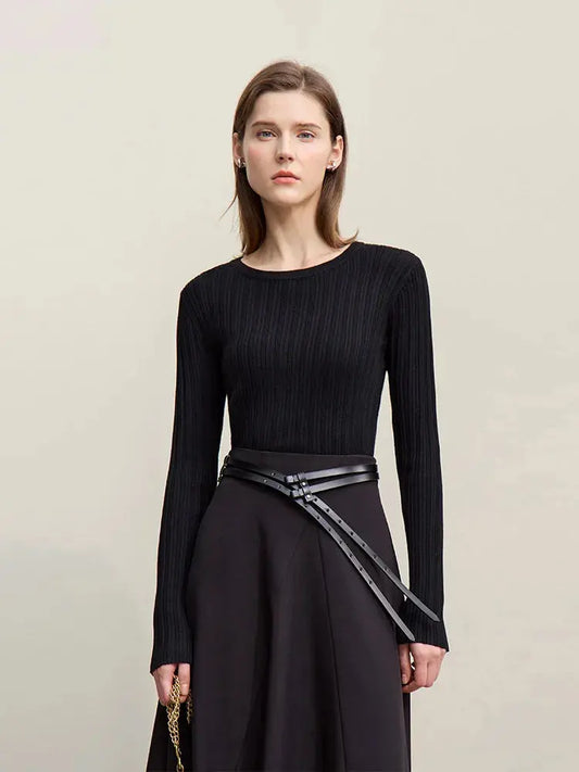 Woman wearing a black ribbed sweater and black skirt with a belt on a beige background