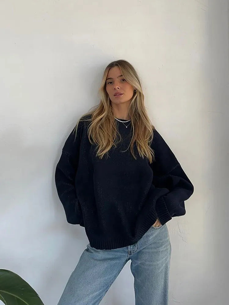 Person wearing a black sweater and light blue jeans against a white wall