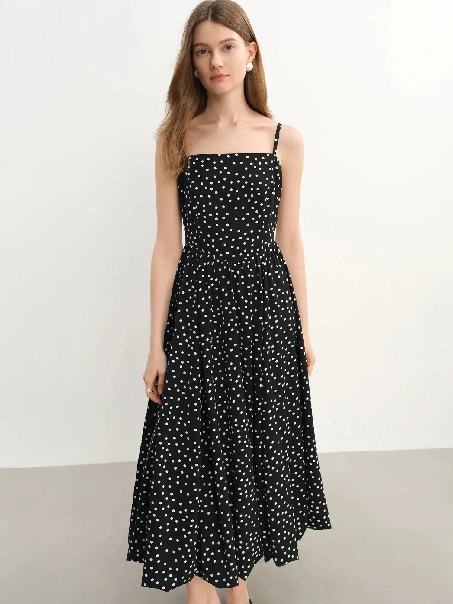 Woman wearing a black dress with white polka dots on a plain background