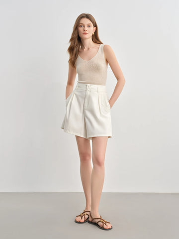 Woman wearing a beige sleeveless top and white shorts on a plain background