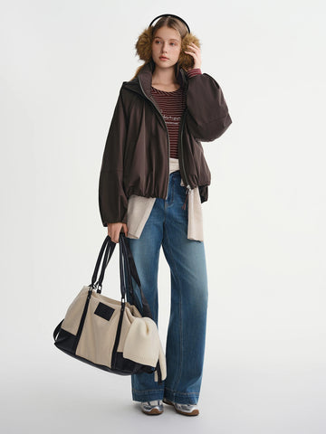 Person wearing a brown jacket, blue jeans, and holding a beige and black bag on a white background