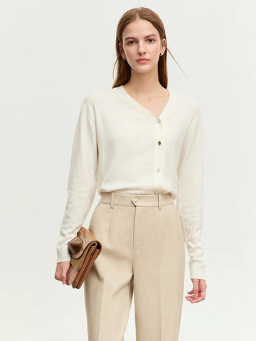 Woman wearing a white cardigan and beige pants holding a brown clutch against a white background