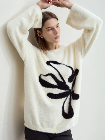 Woman wearing a white sweater with a black butterfly design against a plain background