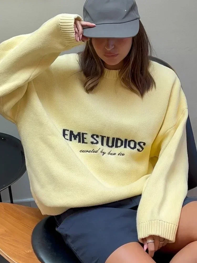 Person wearing a yellow 'EME STUDIOS' sweater sitting on a chair.