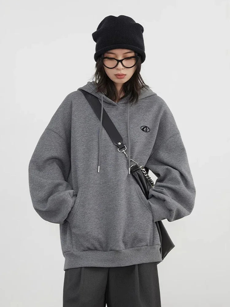 Person wearing a gray hoodie with a small logo, black beanie, and glasses on a white background