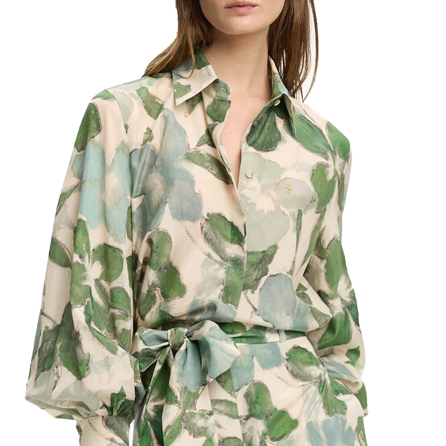 Woman wearing a floral patterned blouse with green and blue leaves on a white background