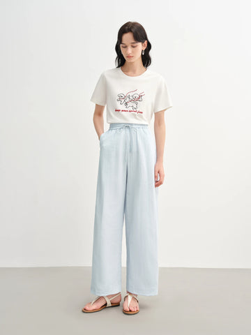 Woman wearing a white t-shirt with a graphic design and light blue wide-leg pants on a white background