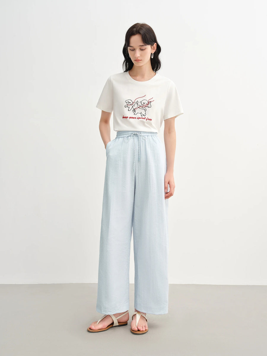 Woman wearing a white t-shirt with a graphic design and light blue wide-leg pants on a white background