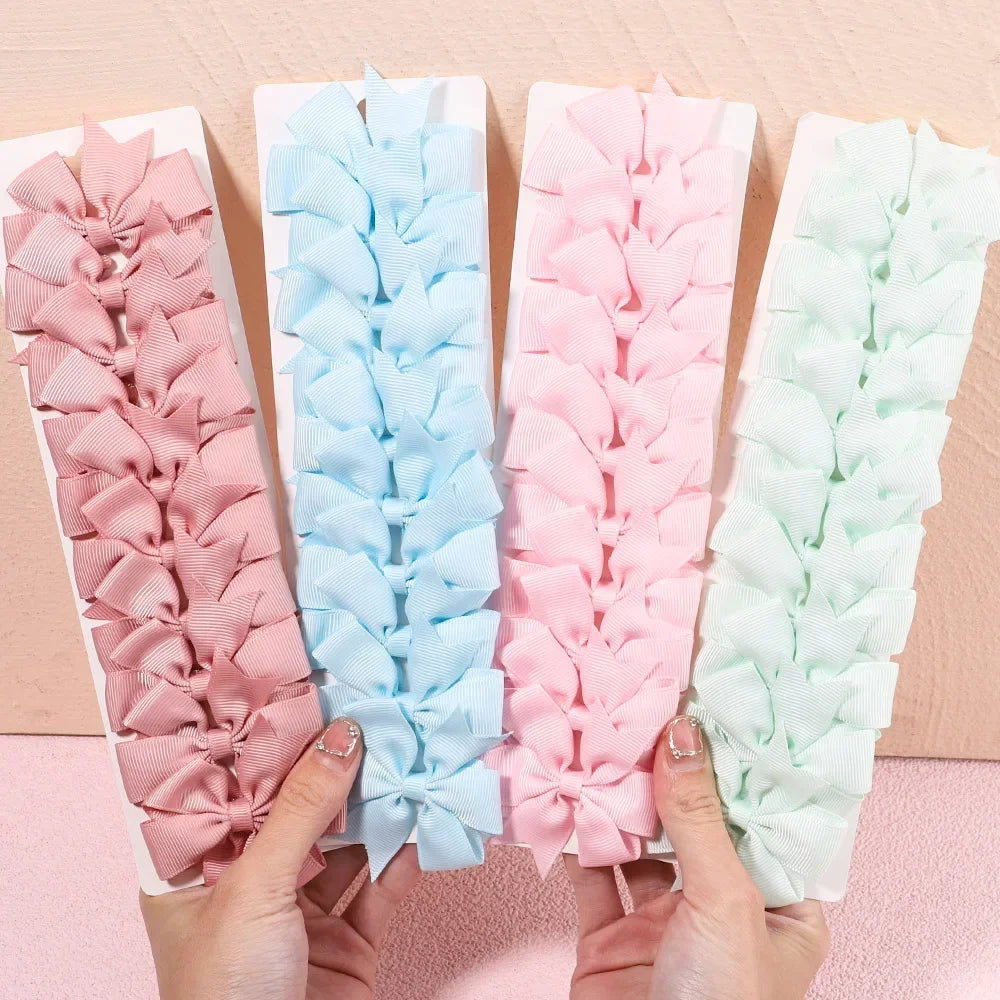 Four trays of colorful hair bows held by hands on a pink surface