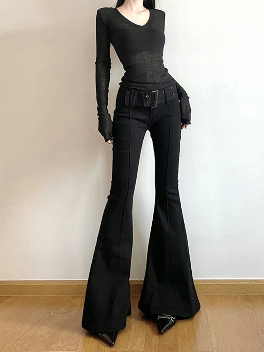 Person wearing a black outfit with bell-bottom pants on a plain background