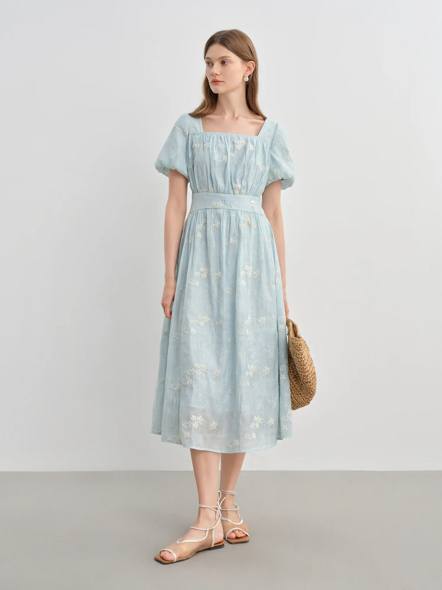 Woman wearing a light blue dress with a white floral pattern against a plain background