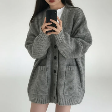 Person wearing a gray cardigan taking a mirror selfie.