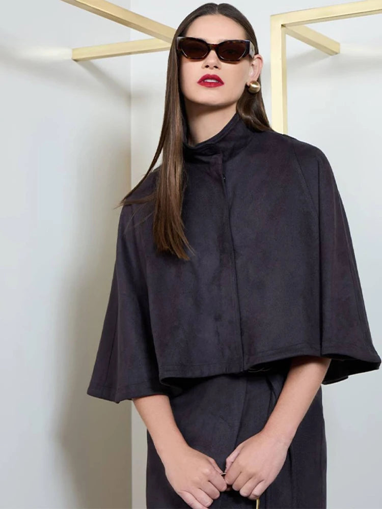 Woman wearing a black cape and sunglasses against a white background