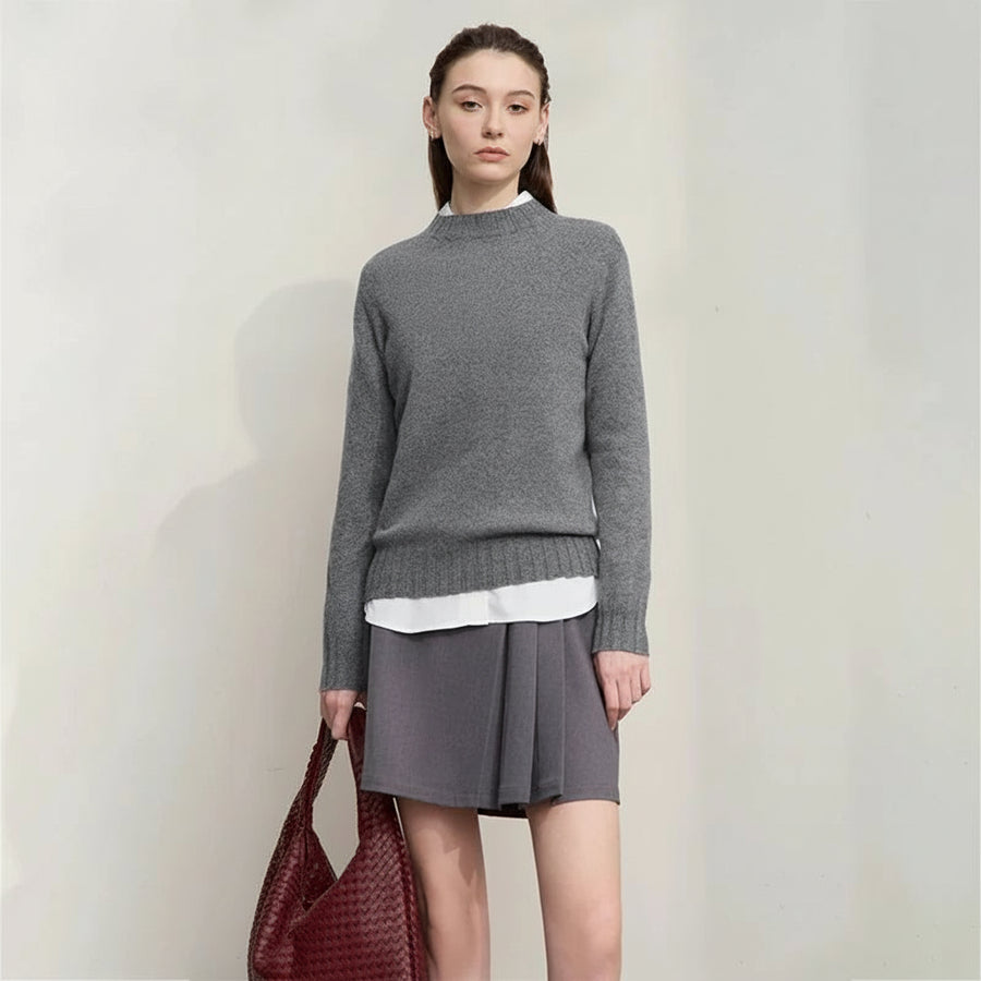 Woman wearing a gray sweater and skirt with a white shirt underneath, holding a red bag on a plain background.