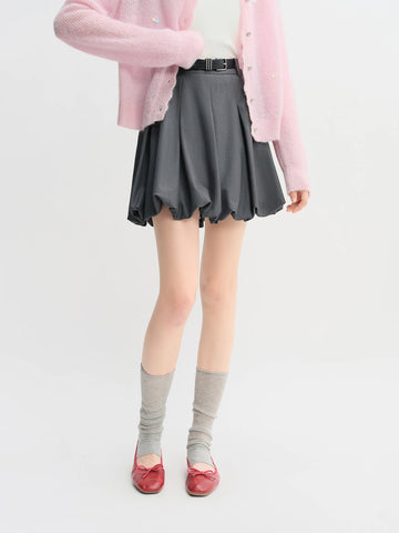 Person wearing a pink cardigan, gray pleated skirt, gray socks, and red shoes on a white background