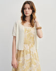 Woman wearing a yellow floral dress with a white cardigan on a plain background