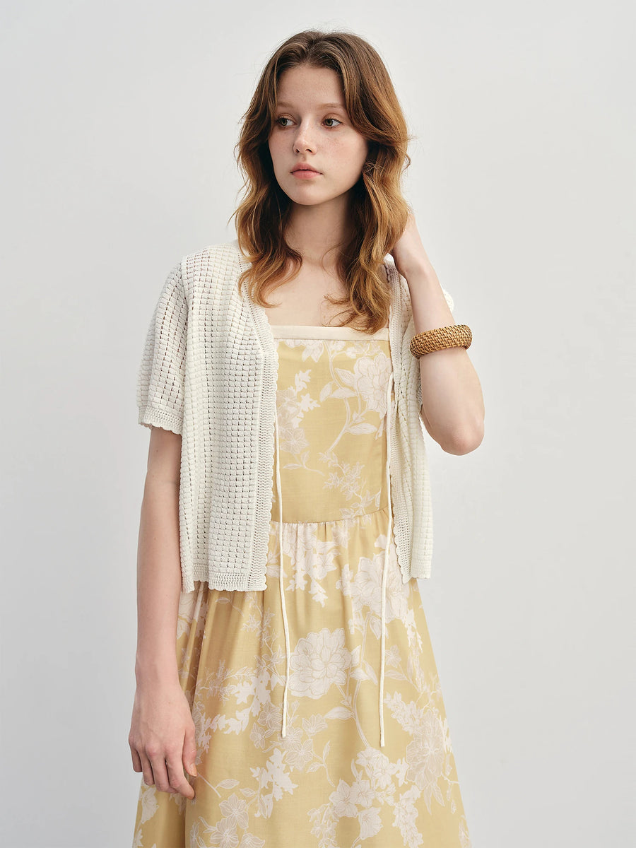 Woman wearing a yellow floral dress with a white cardigan on a plain background