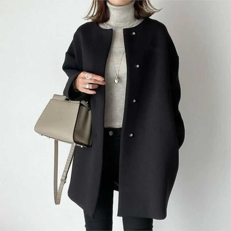 Person wearing a black coat holding a beige handbag on a plain background