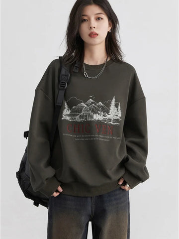 Person wearing a dark green sweatshirt with a graphic design and text, standing against a plain background.