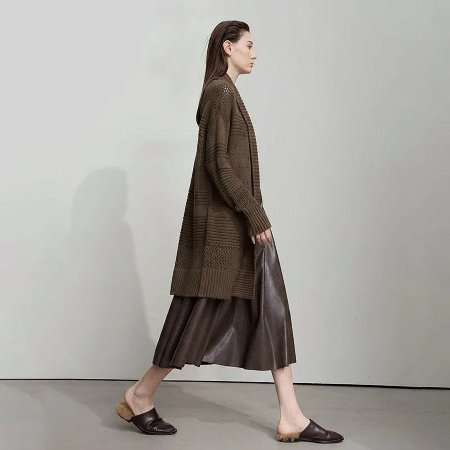 Woman wearing a long brown cardigan and skirt with 'Amii' branding.