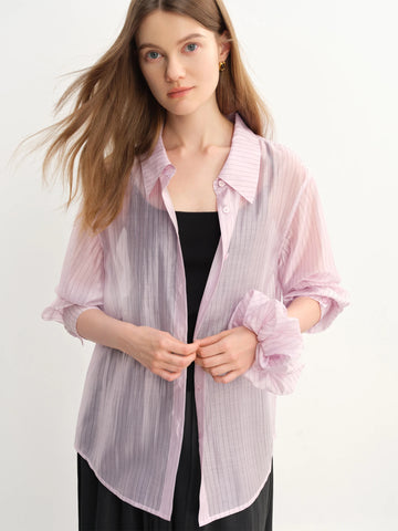 Woman wearing a light pink sheer blouse over a black top on a white background