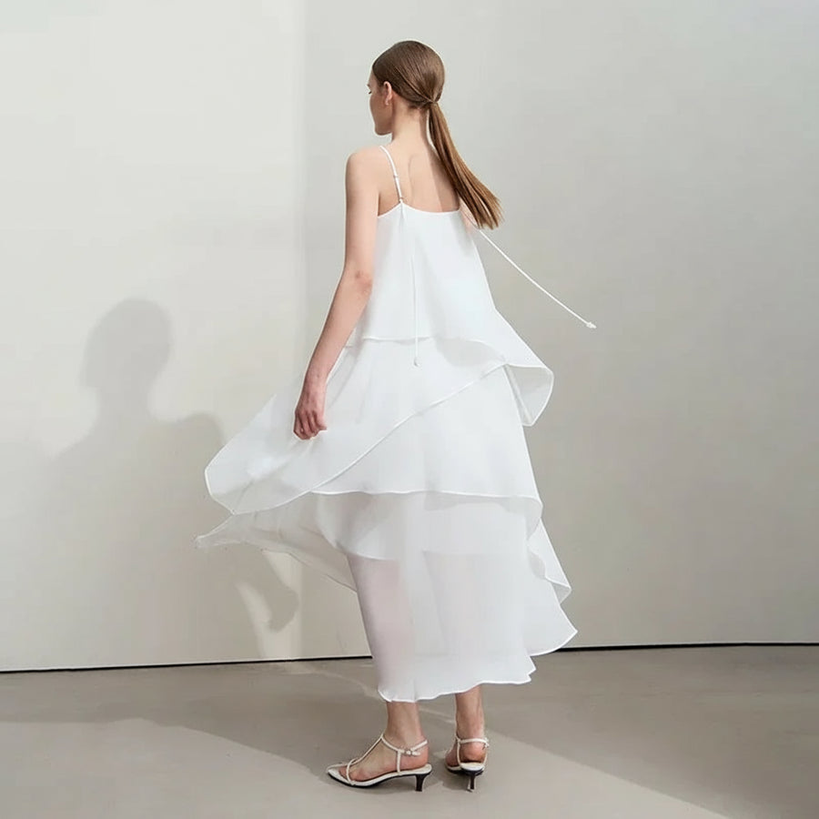 Woman wearing a white dress with ruffled layers, standing against a plain background. Brand 'Amii' visible.