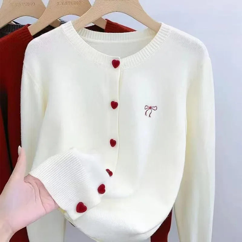 White sweater with red heart buttons held by a hand against a neutral background