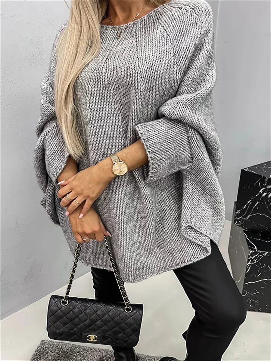 Person wearing a gray oversized sweater and black pants, holding a black quilted handbag.