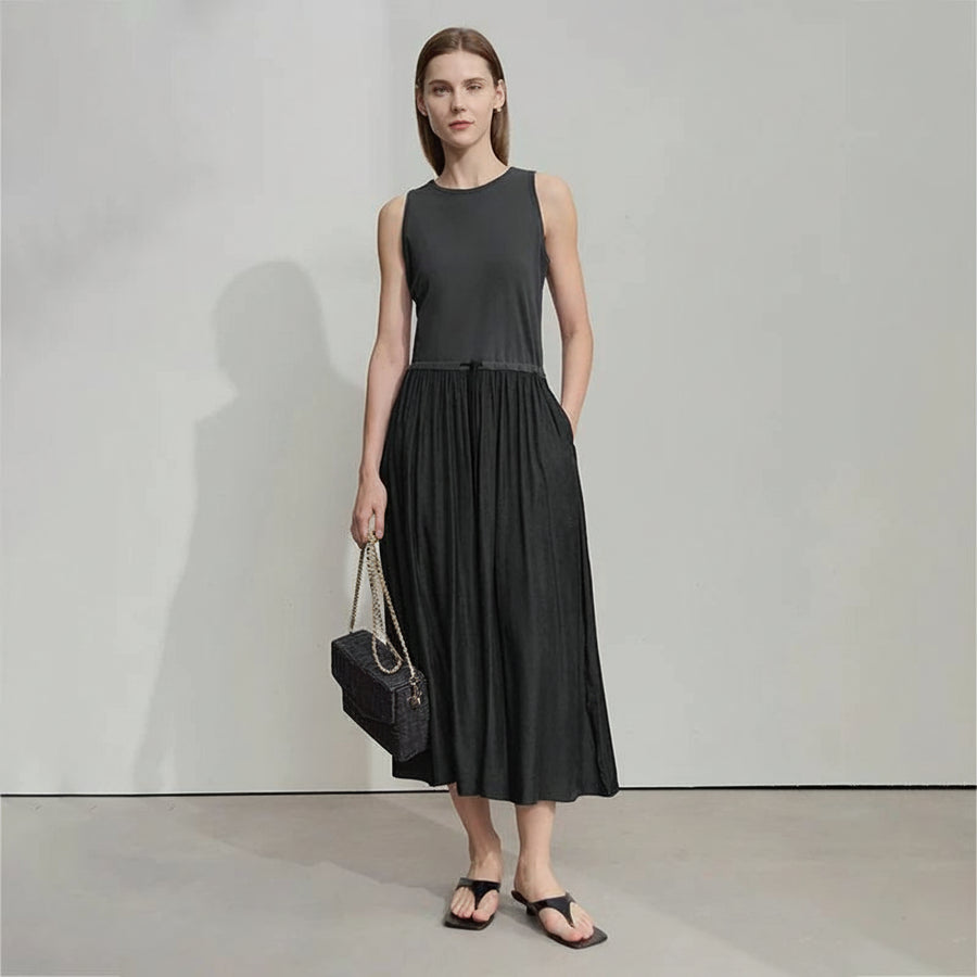 Woman wearing a black sleeveless dress with a plain background, featuring the brand 'Amii'.