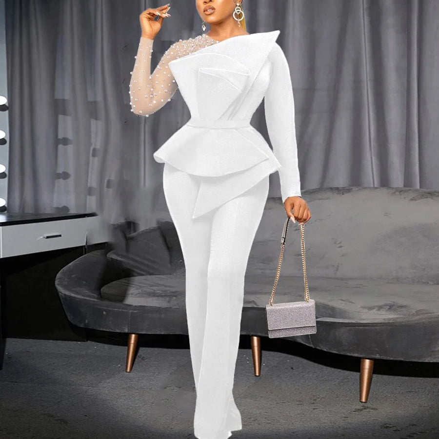 Woman in a white outfit holding a handbag in a room with gray curtains and furniture.