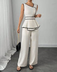 Woman wearing a white and black peplum top with wide-leg pants against a gray curtain background.