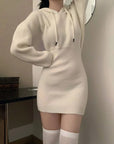 Person wearing a white knit dress with a hood in a room.