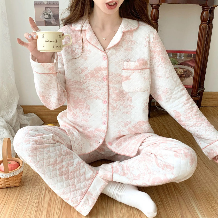 Person wearing pink quilted pajamas holding a mug indoors.