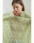 Woman wearing a green lace sweater with 'AMII' branding.
