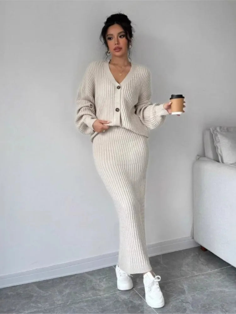 Woman in a beige ribbed sweater and pants holding a coffee cup indoors.