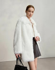 Woman wearing a white fur coat with a plain background, featuring the brand 'Amii'.