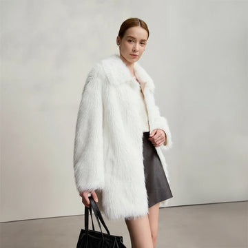 Woman wearing a white fur coat with a plain background, featuring the brand 'Amii'.