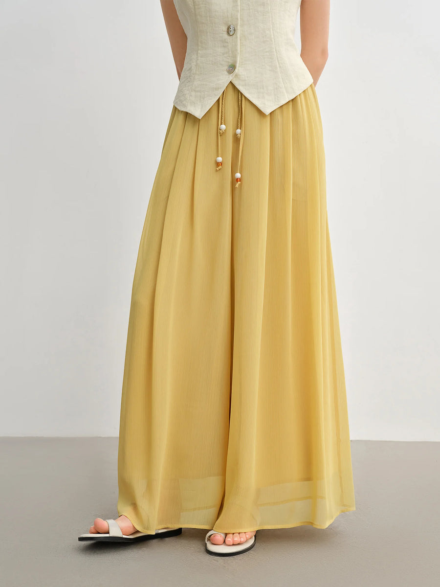 Person wearing a long mustard yellow skirt with a white top on a plain background